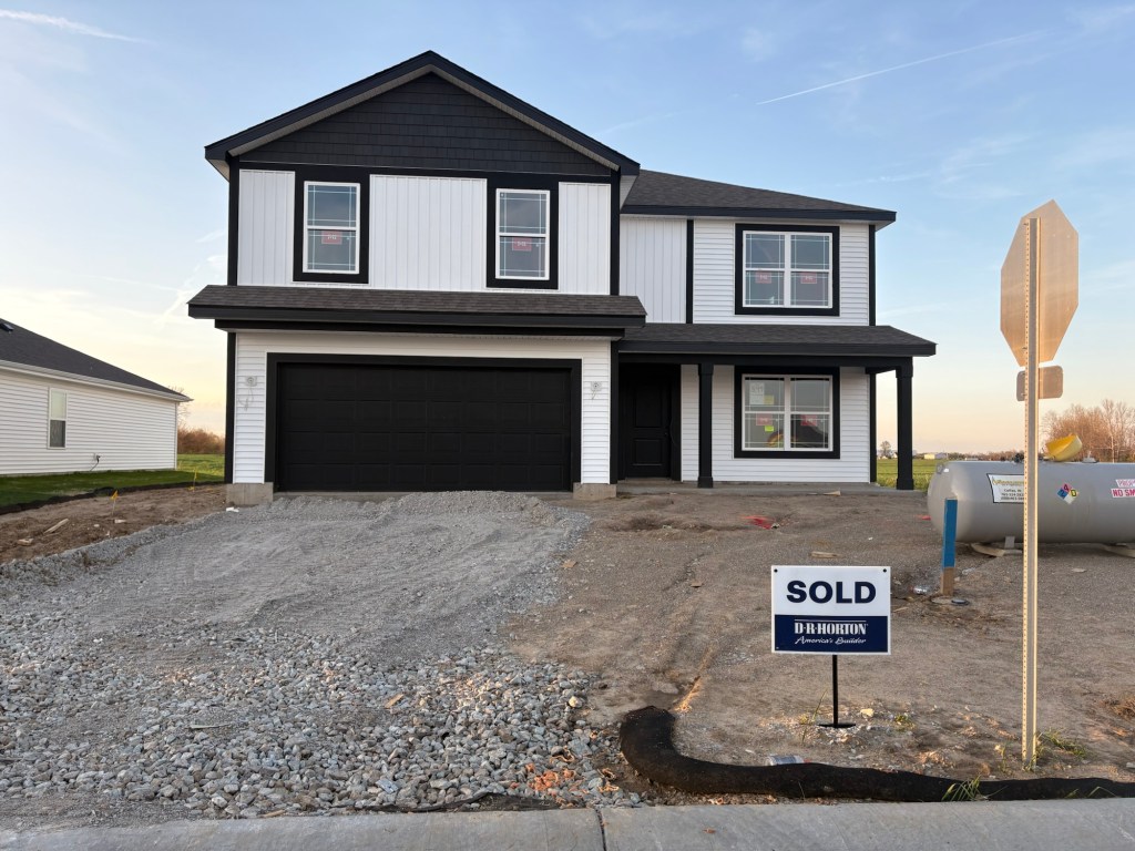 A newly built two-story house with a black and white exterior design, featuring a sold sign in front. The house has multiple windows with construction details visible inside.