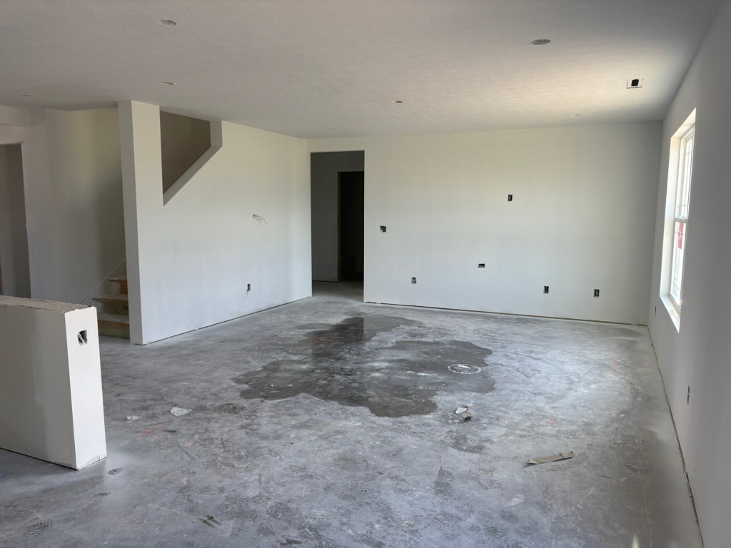 Interior of an unfinished house with bare walls, concrete floor, and visible electrical outlets.